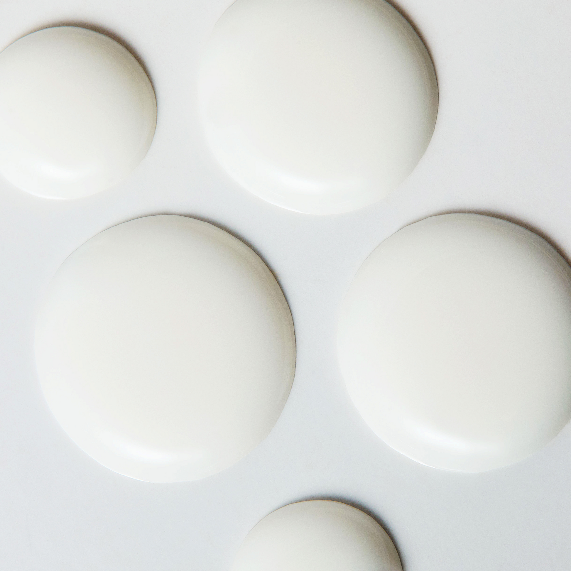 Close up image showing several smooth, glossy white cream drops on a light surface, representing the texture and consistency of a skincare product.