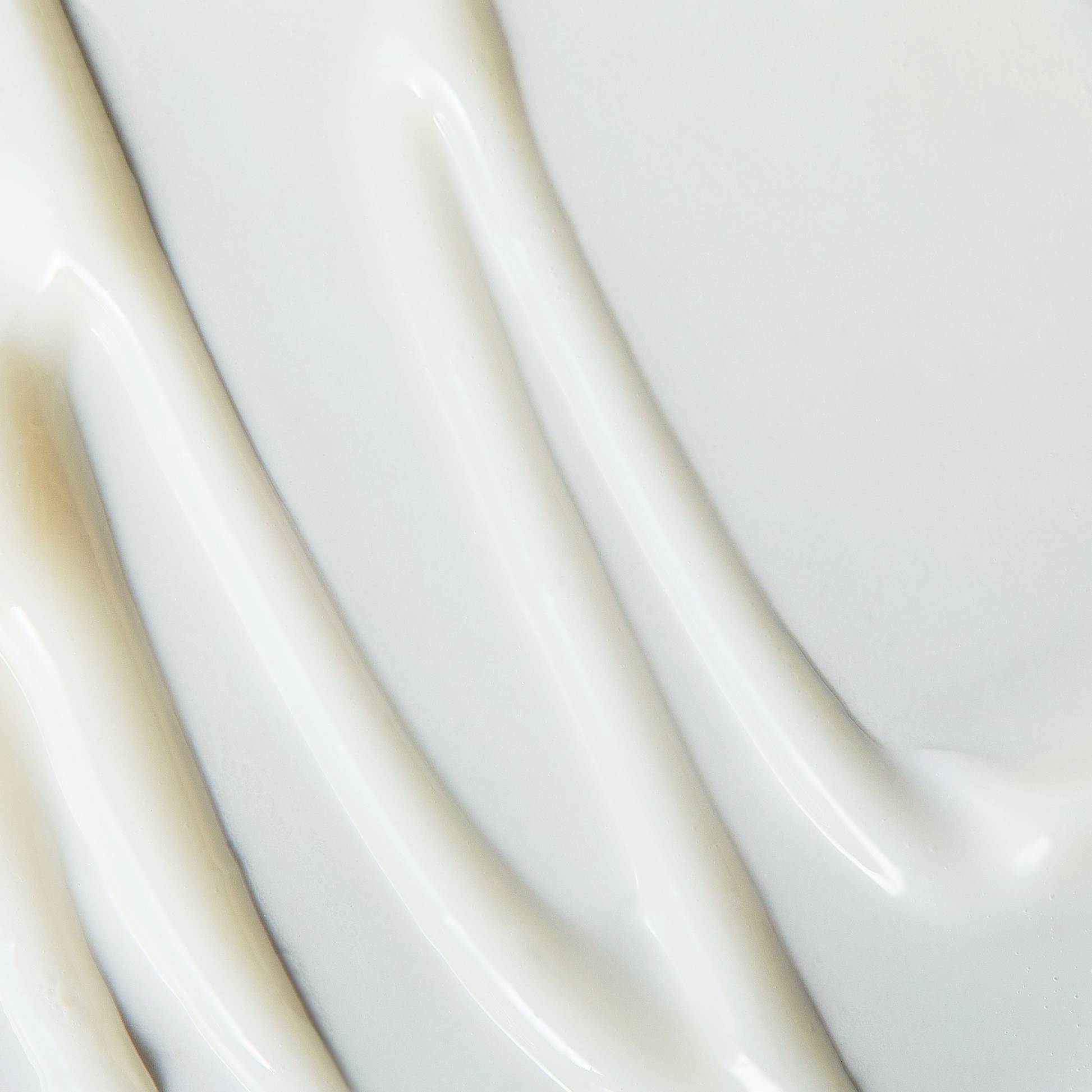 Close-up texture image of a creamy white skincare product spread in smooth diagonal streaks. The glossy surface highlights its rich, hydrating consistency.