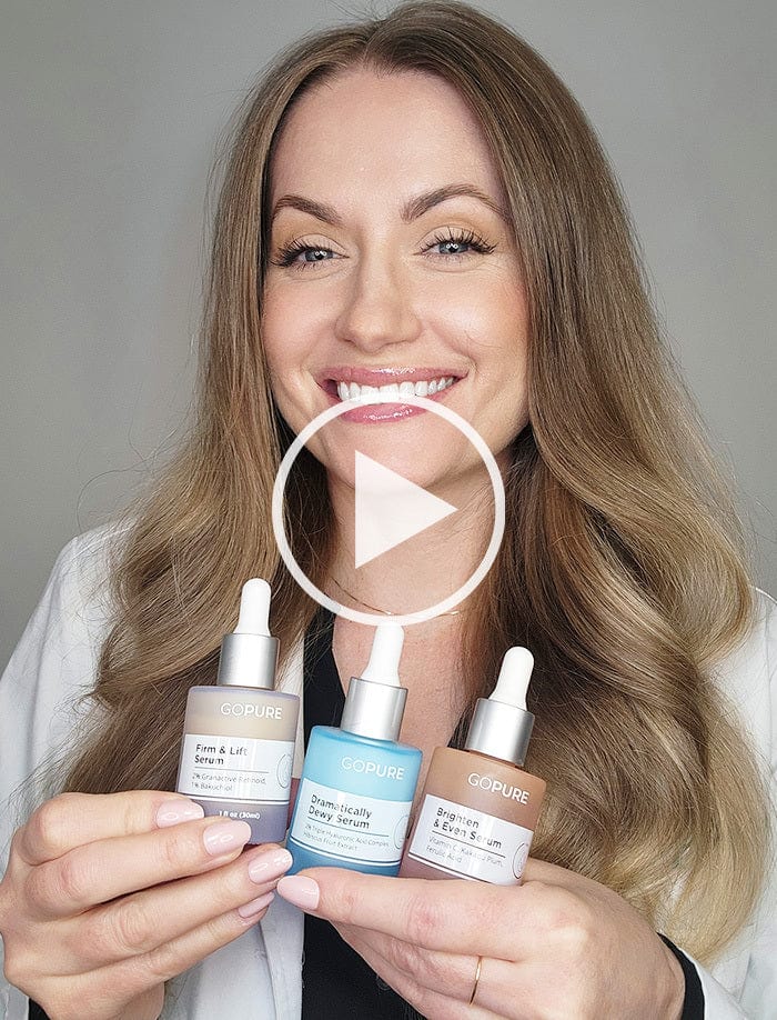 Smiling woman with long blonde hair holding three GoPure skincare serums: Firm & Lift Serum, Dramatically Dewy Serum, and Brighten & Even Serum. A play button icon is overlaid on the image, indicating a video.