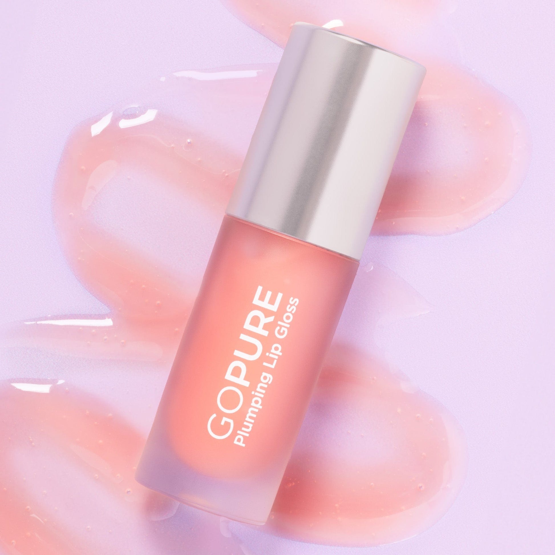 A GoPure Plumping Lip Gloss bottle on a lavender background, surrounded by glossy, peach-toned lip gloss smears. The product is labeled “GOPURE Plumping Lip Gloss.”