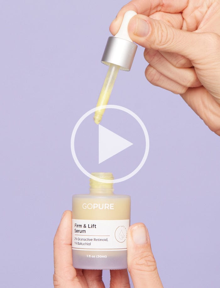 Hand holding a dropper above a bottle of GoPure Firm & Lift Serum against a light purple background. The bottle label highlights ingredients including 2% Granactive Retinoid and 1% Bakuchiol.