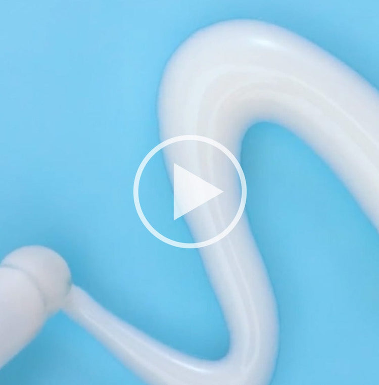 White cream being dispensed in a wavy line on a blue surface. A play button icon is overlaid on the image, indicating a video.