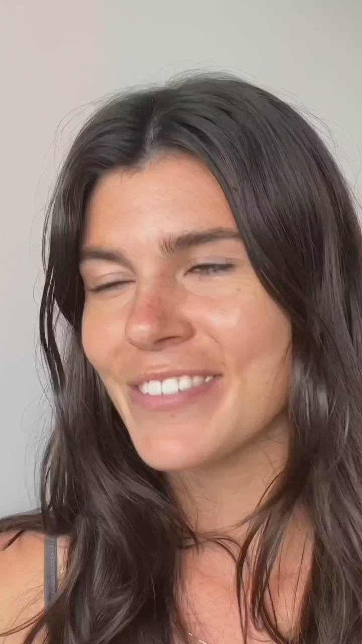 Woman with long dark hair smiling with her eyes closed, against a plain background.