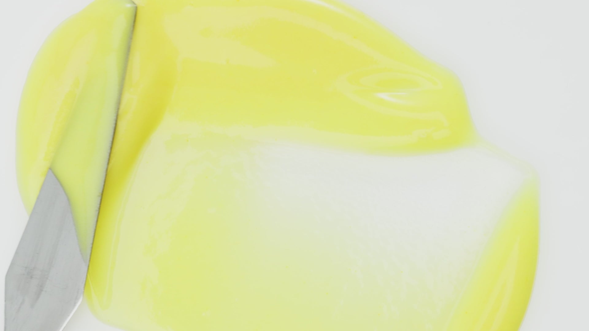 A close-up of yellow skincare serum being spread with a spatula on a white surface.